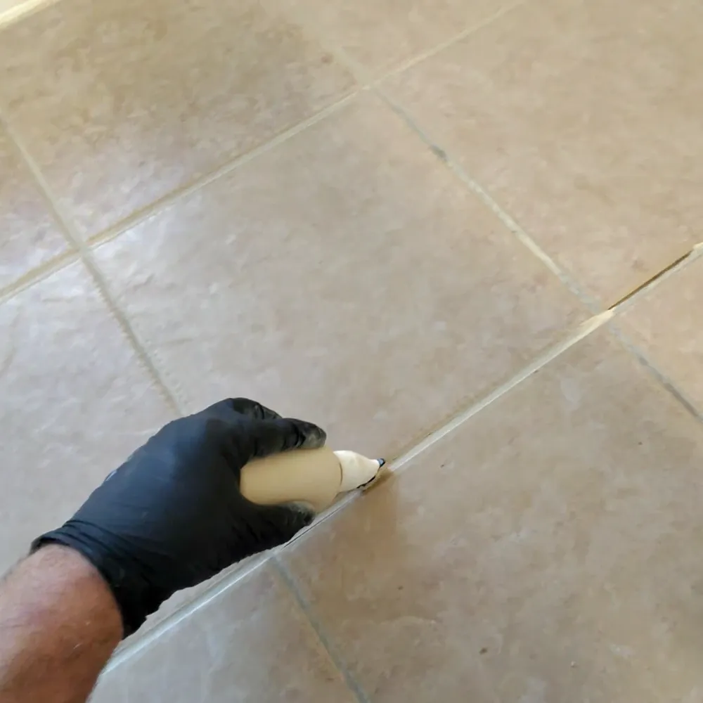 Technician hand-applying grout color sealant along a grout line