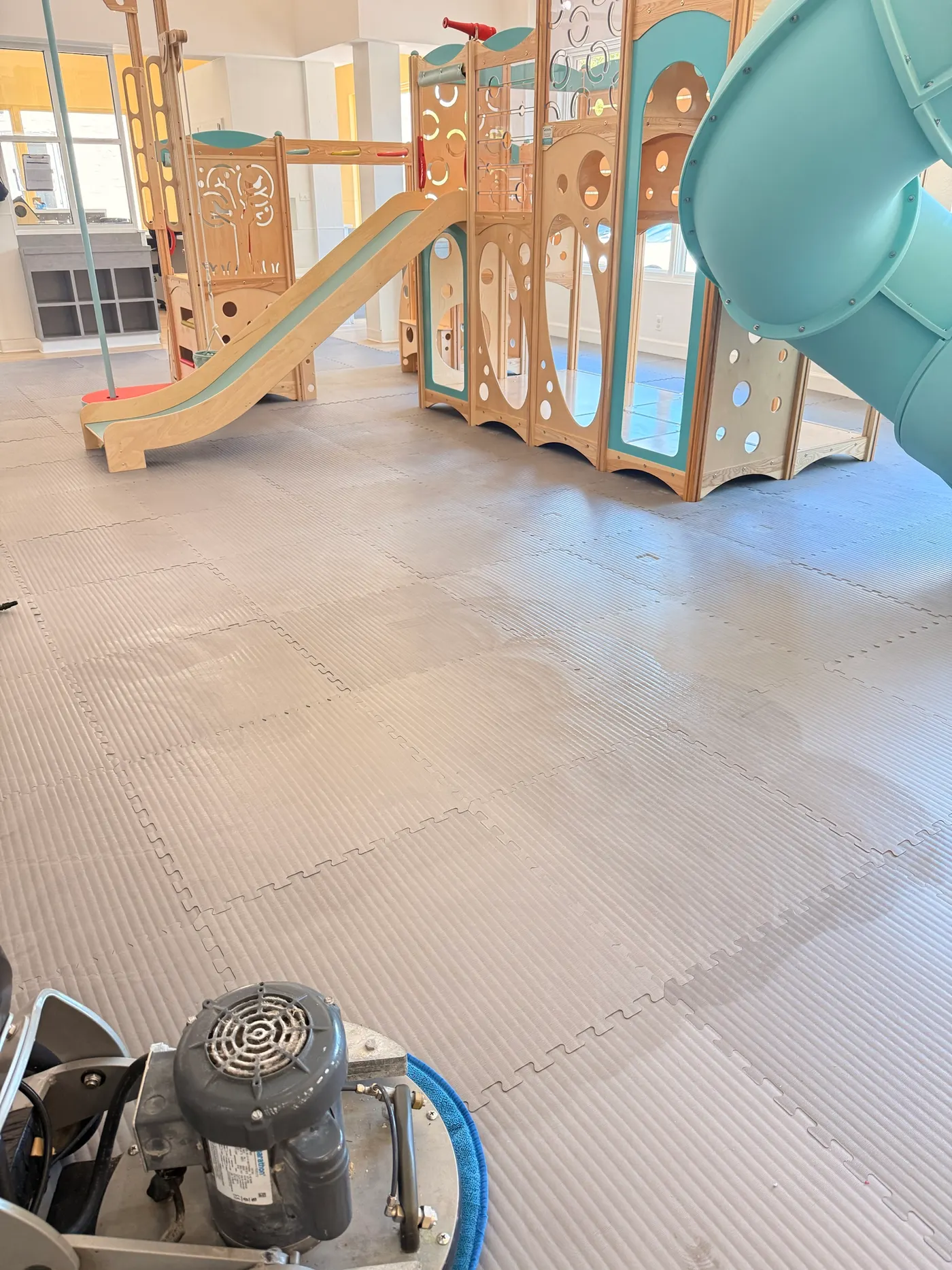 Floor machine with a microfiber pad cleaning foam play mats under an indoor playground in a Southlake daycare