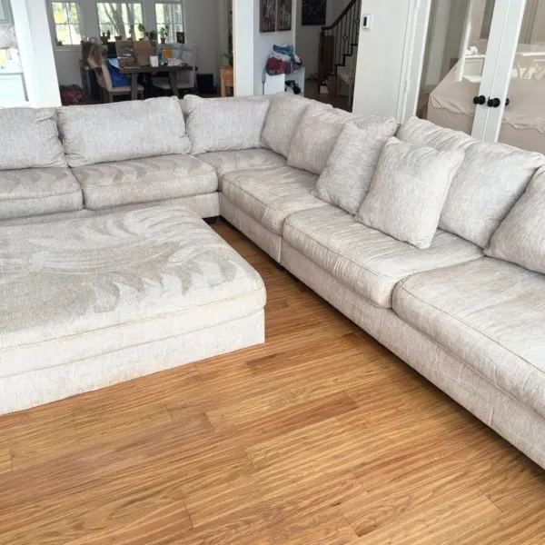 Cream sectional and ottoman midway through upholstery cleaning