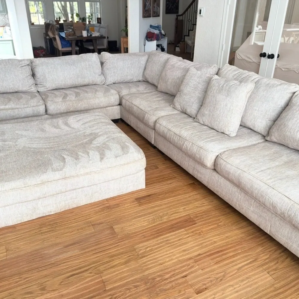 Cream sectional and ottoman midway through upholstery cleaning